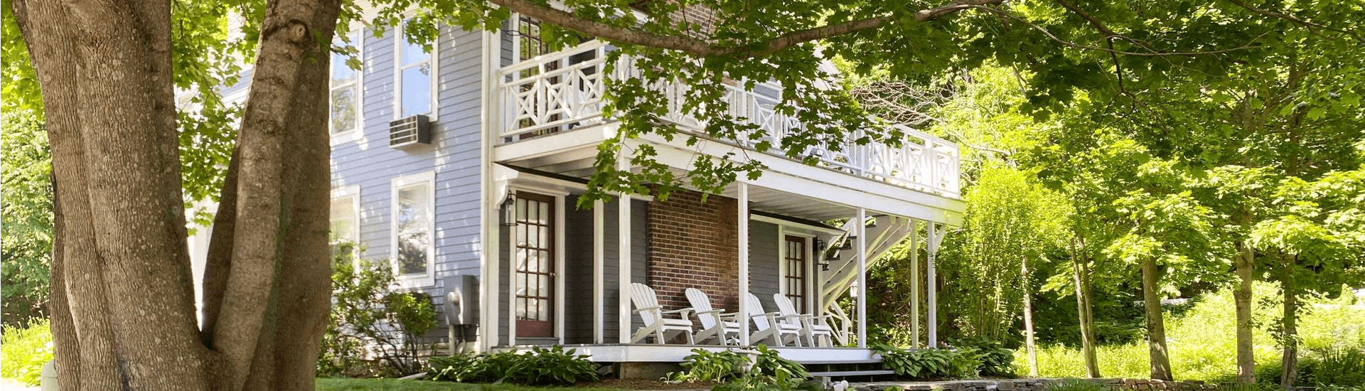 A two-story house with a porch, surrounded by lush greenery and trees.