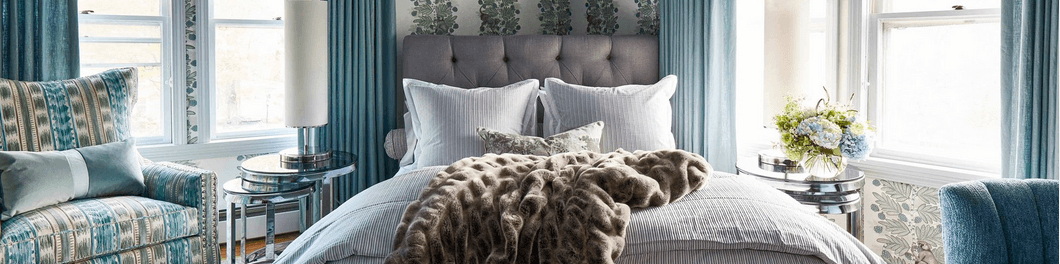 A stylish bedroom featuring a plush bed, patterned armchair, and floral decor with soft blue accents.