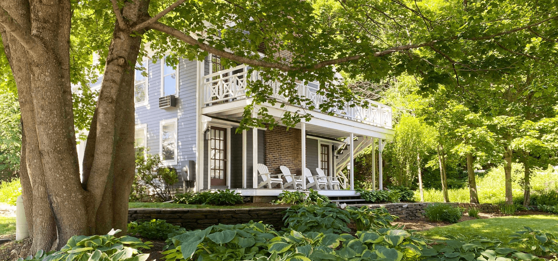 A charming two-story house with a porch surrounded by lush greenery.