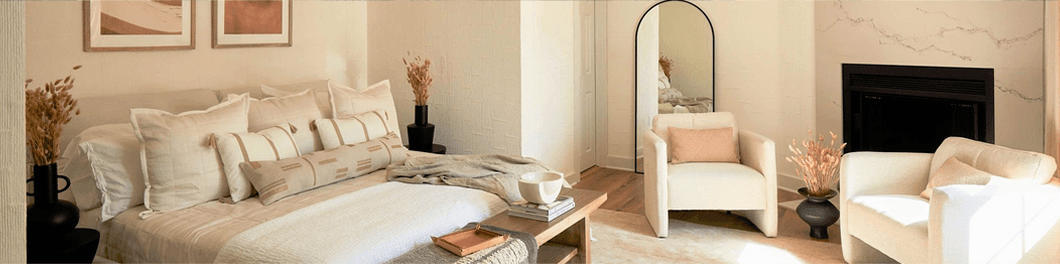 A cozy, modern bedroom featuring a bed with layered pillows, a stylish armchair, and a mirror, accented by minimalist decor and soft lighting.