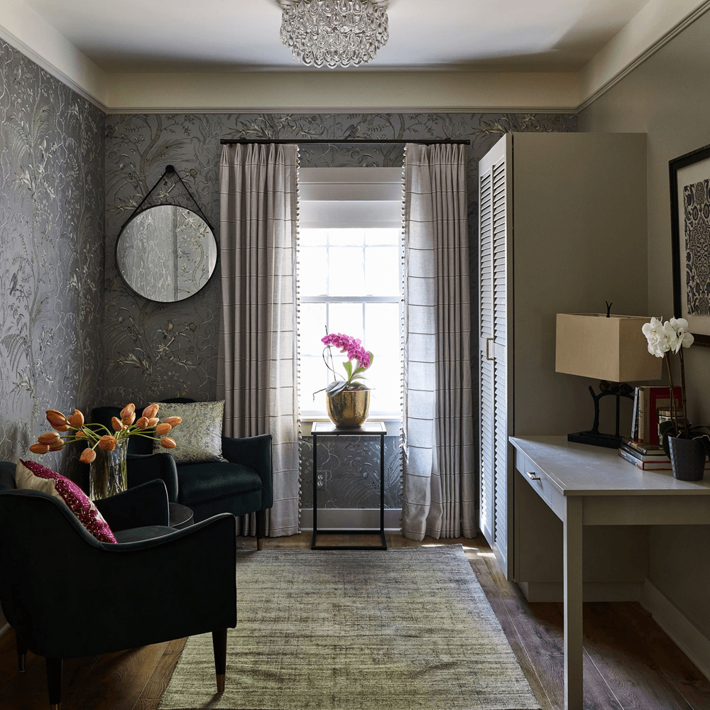 A cozy, elegantly decorated room featuring a green armchair, a small table with flowers, a window, and tasteful wall decor.